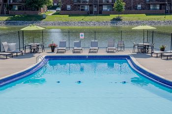 a swimming pool with chairs and umbrellas and a lake in the background